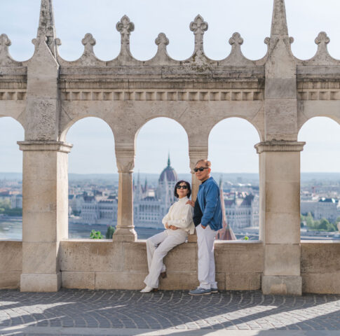 Elegant senior couple posing in front of the arches of the Fisherman's Bastion overlooking the Budapest Parliament.